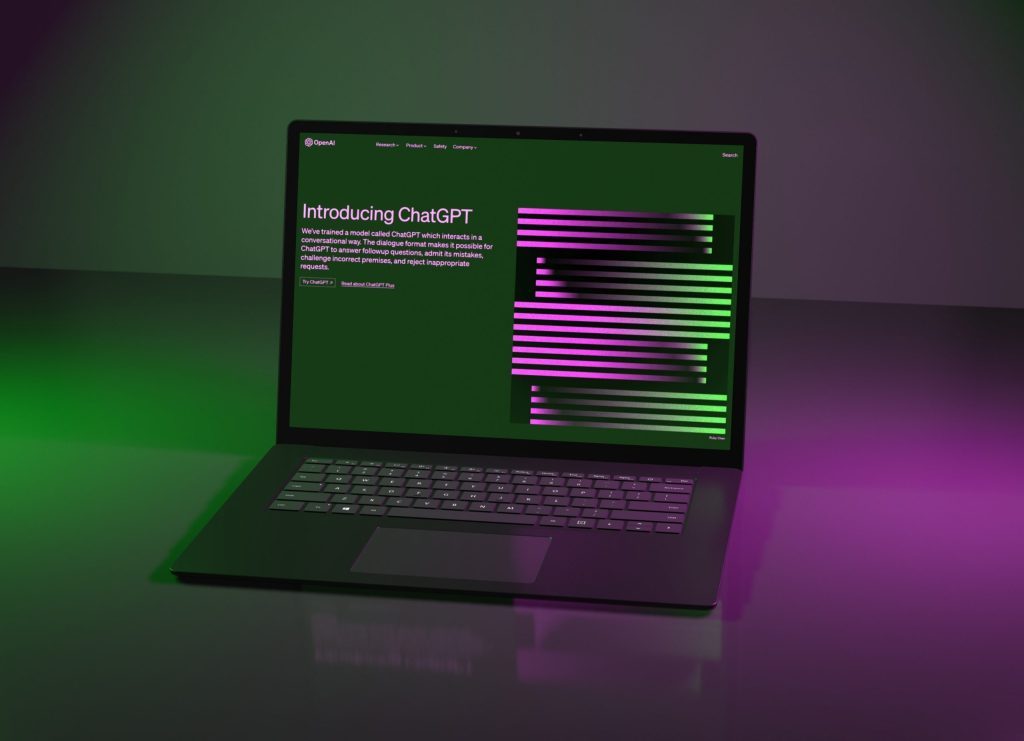 A laptop displaying a dark green screen with the title "Introducing ChatGPT" and text explaining the model's capabilities, set against a backdrop of purple and green lighting.